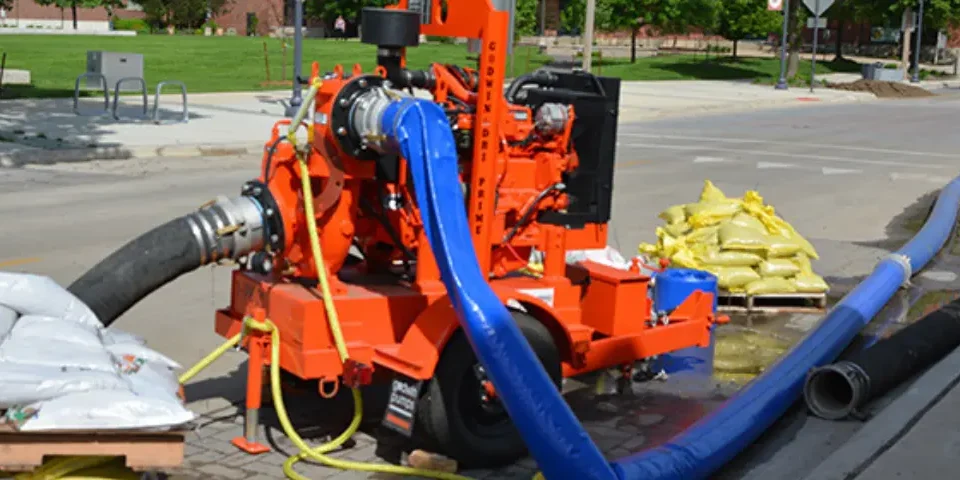 Large orange industrial pump with suction hoses and discharge hoses