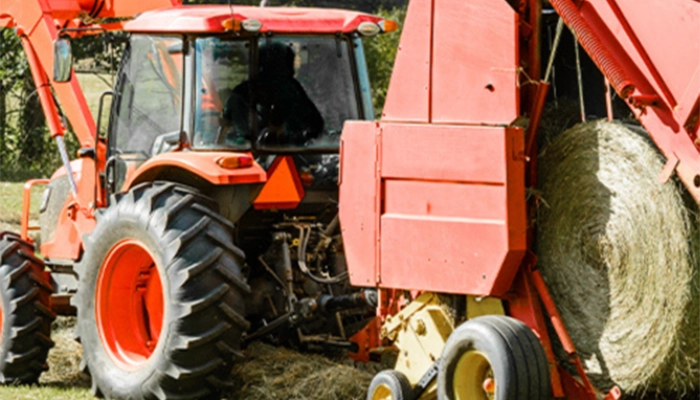 Close-up image of a tractor using baler belting to round hay bailing