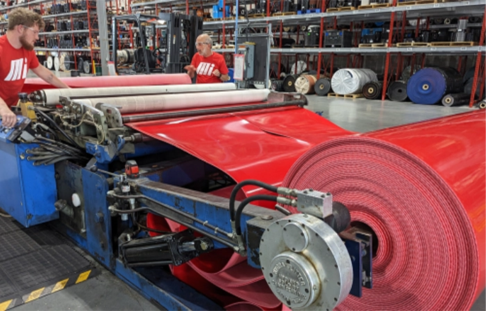 Motion Conveyance technicians wearing protective goggles while fabricating a large custom red belt in facility