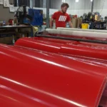 Two male Motion Conveyance technicians fabricating a large red conveyor belt in facility