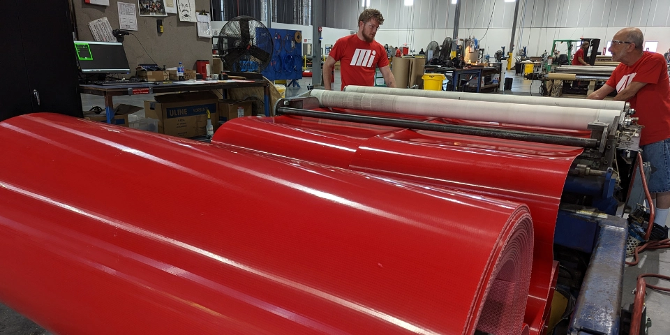 Two male Motion Conveyance technicians fabricating a large red conveyor belt in facility