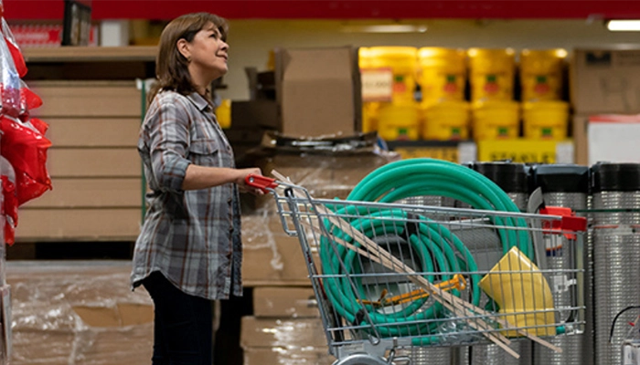 Female customer pushing shopping cart with green hoses in home improvement retail location