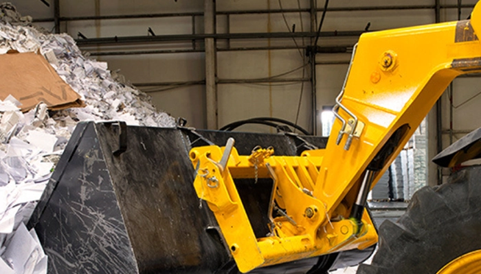 Yellow heavy wheeled excavator moving pile of recycling in recycling facility