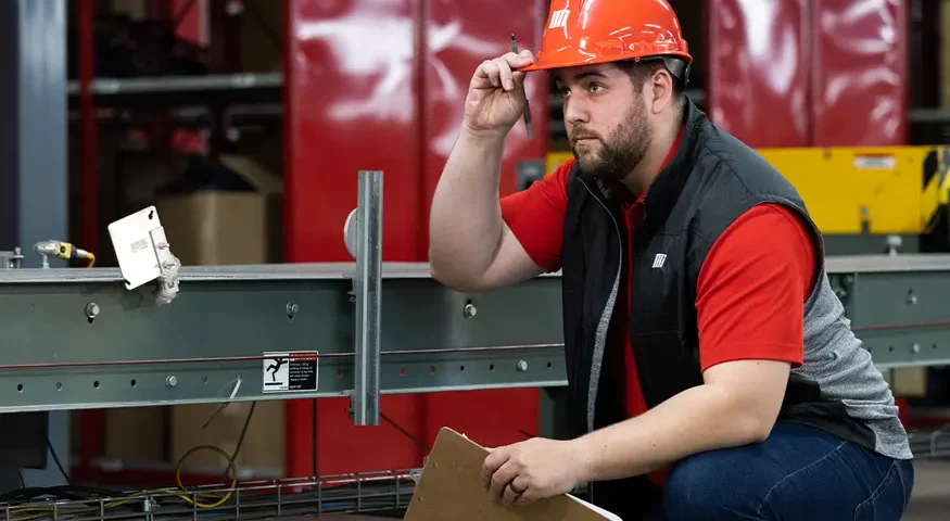 Motion Conveyance technician wearing personal protective equipment (PPE) and holding a clip board on site