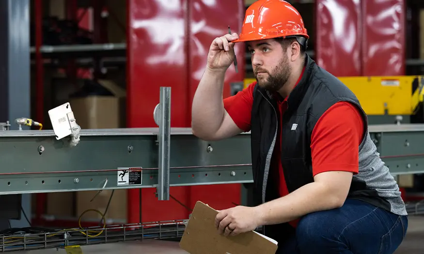 Motion Conveyance technician wearing personal protective equipment (PPE) and holding a clip board on site