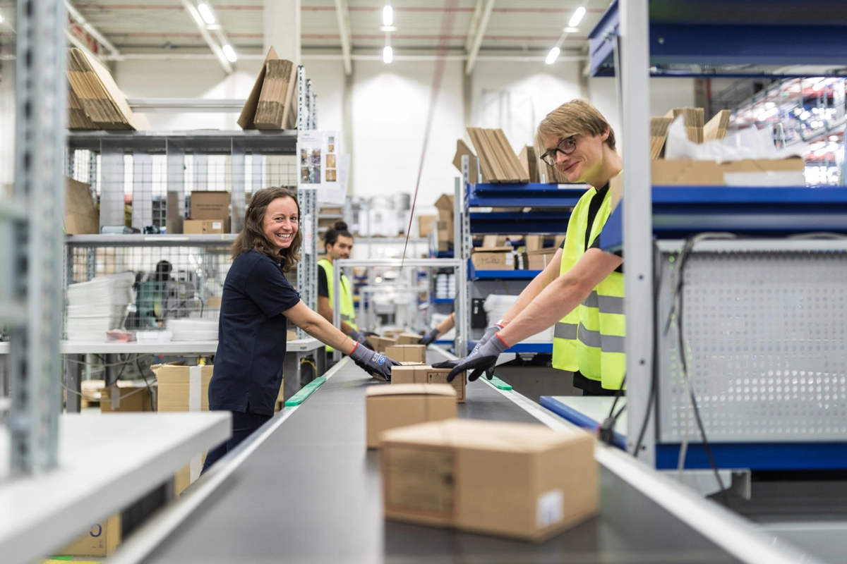 Smiling workers working on conveyor belt line in a distribution warehouse