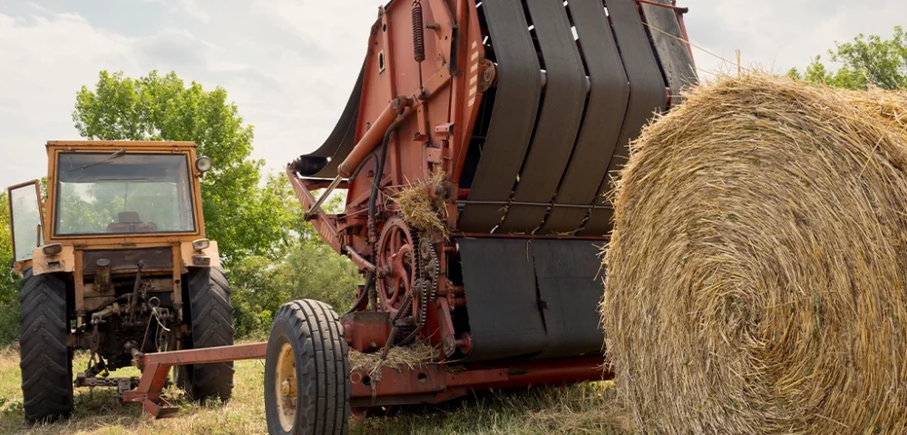 Large tracker and hay baler, baling hay on farm with gray sky in the background