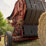 Large tracker and hay baler, baling hay on farm with gray sky in the background