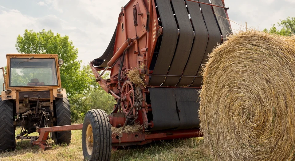 Large tracker and hay baler, baling hay on farm with gray sky in the background