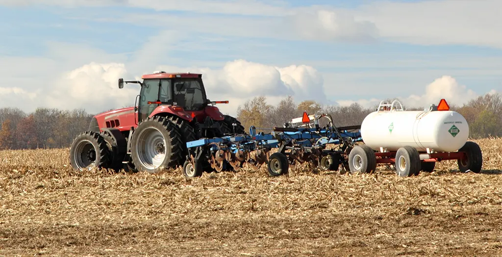 Red tractor pulling plow and anhydrous ammonia tank in a farm field